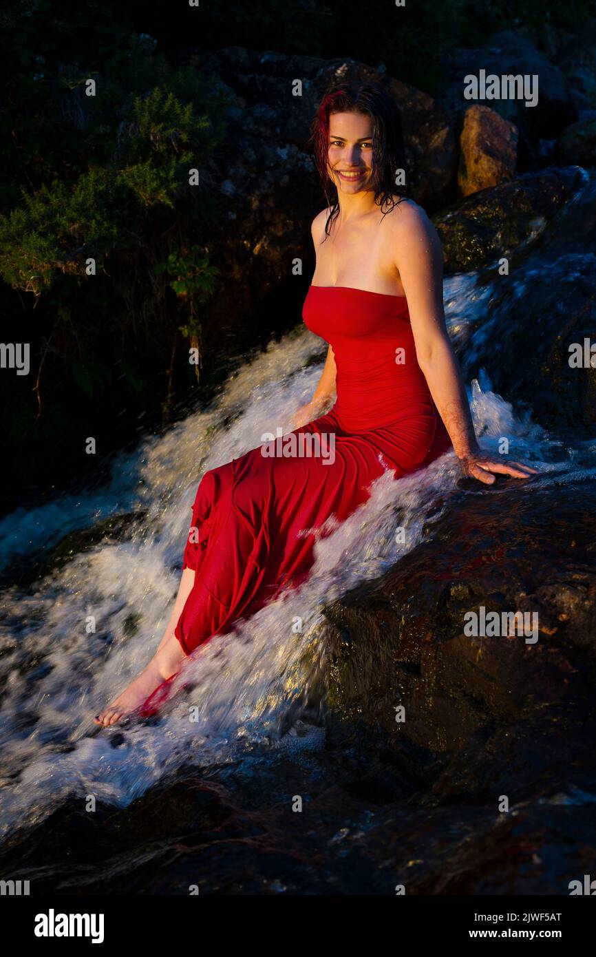 Una hermosa mujer joven con un vestido rojo enfriándose en un río Foto de stock