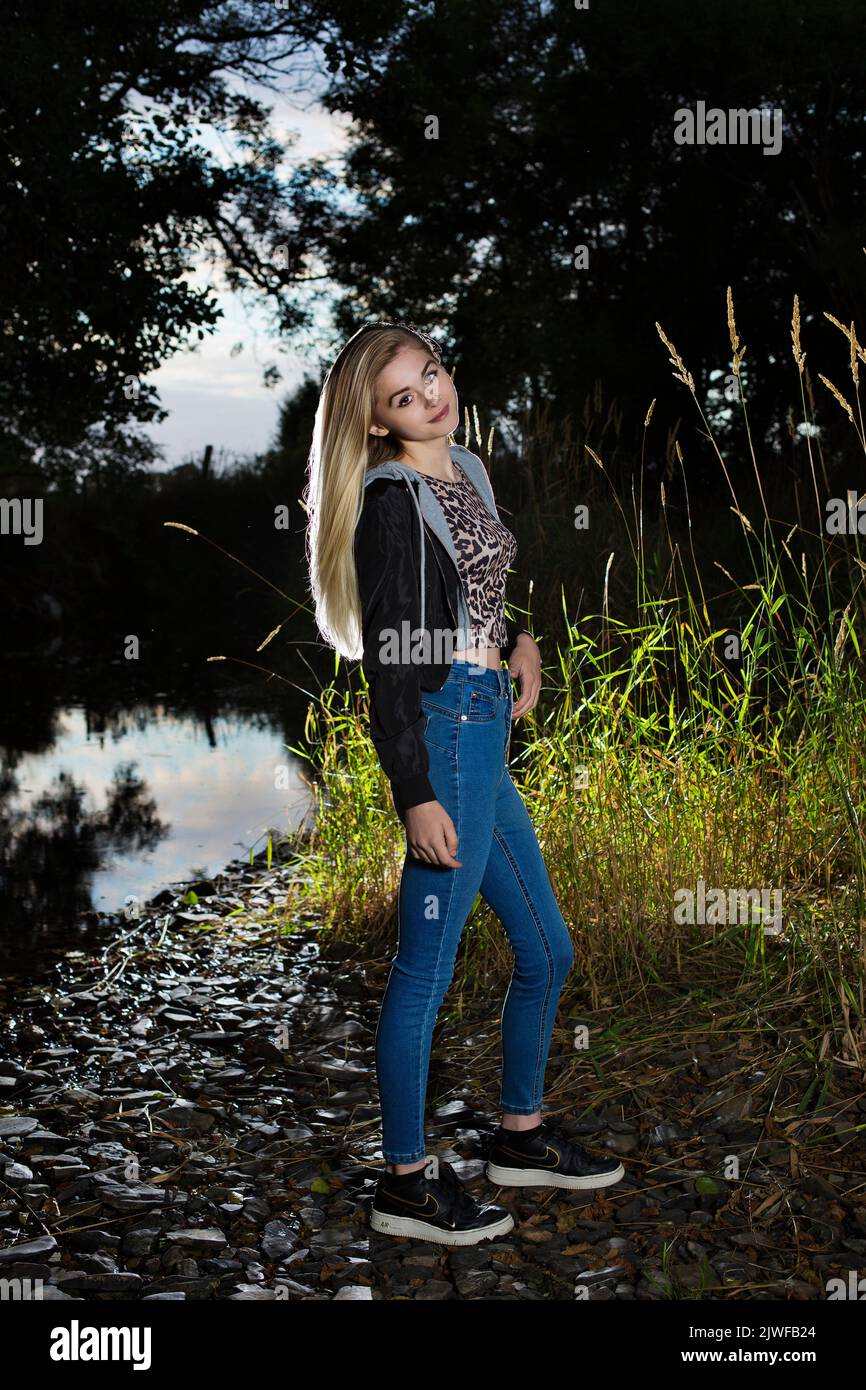 Un adolescente rubio con jeans al aire libre por una orilla del río Foto de stock