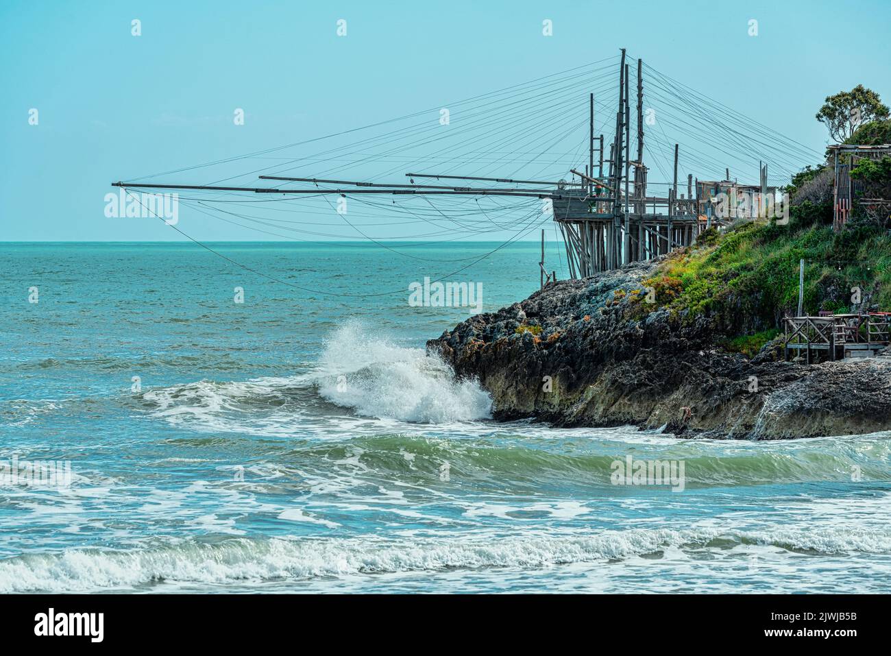 Las olas chocan en los acantilados de la costa de Apulia. Un trebuchet pega sus redes en el mar áspero. Vieste, provincia de Foggia, Puglia, Italia, Europa Foto de stock