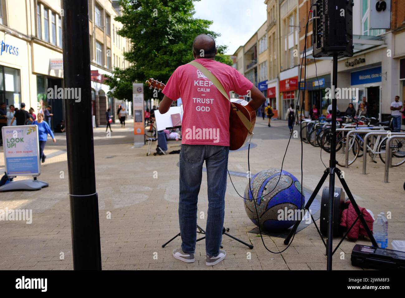 Un cristiano del sur de la India cantando y tocando la guitarra en el centro comercial Broadmead en Bristol, Reino Unido, con una camiseta 'Mantenga la calma y la confianza en dios' Foto de stock