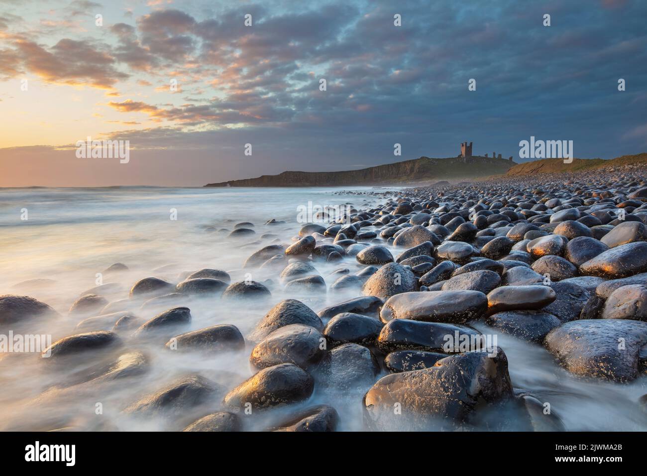 Rompiendo olas en rocas debajo del Castillo de Dunstanburgh al amanecer, Embleton Bay, cerca de Craster, Northumberland, Inglaterra, Reino Unido, Europa Foto de stock