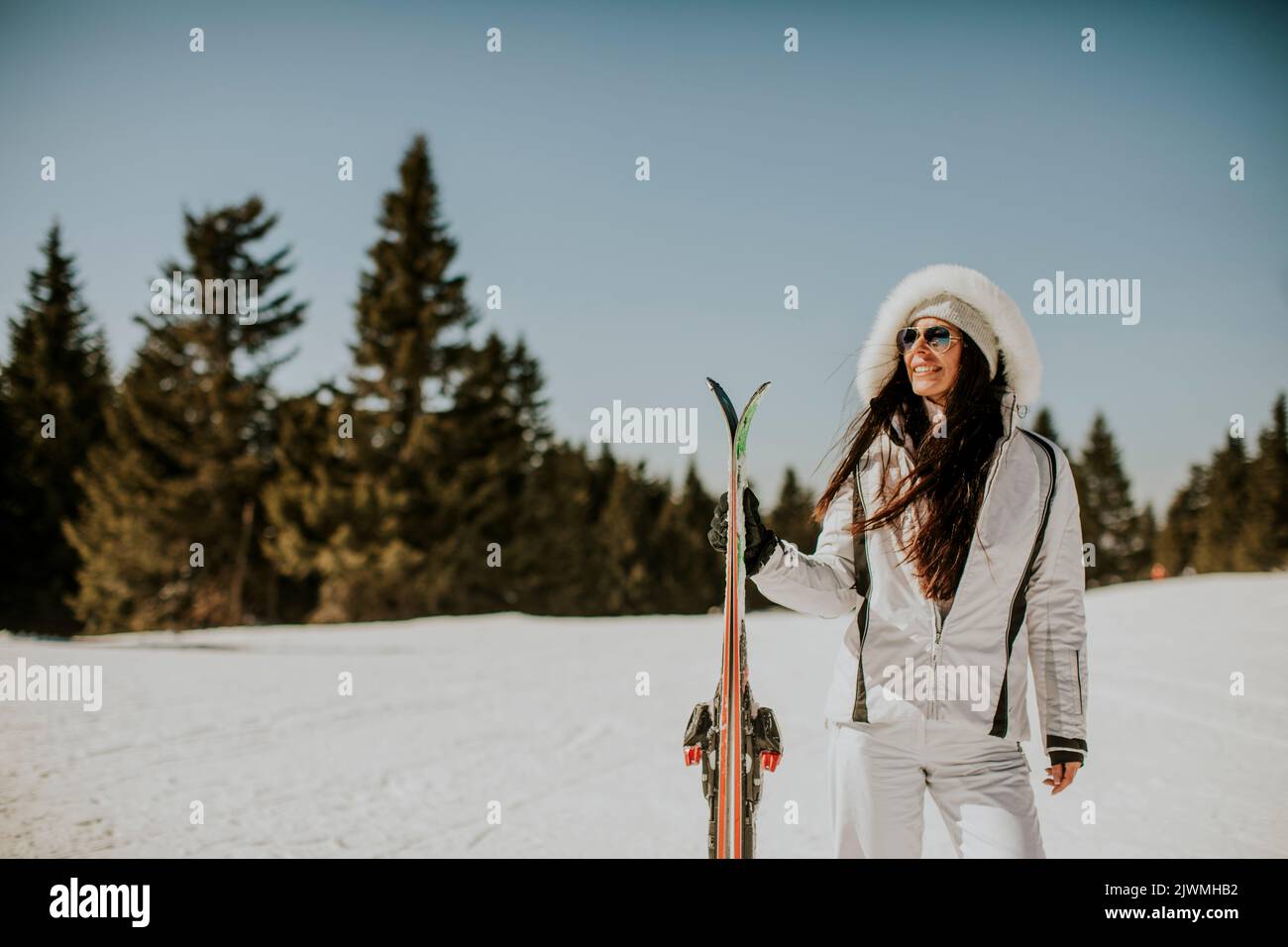 Mujer joven de pie con esquís en la pista de esquí en un día soleado Foto de stock