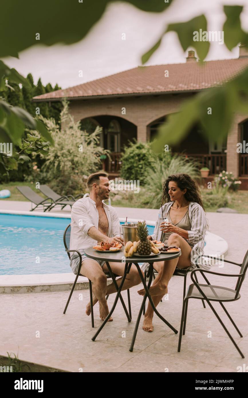 Hermosa pareja joven sentada en el patio trasero, bebiendo lemande y comiendo frutas frescas Foto de stock