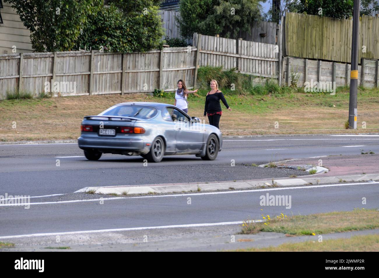 Dos jóvenes turistas se enganchan a hacer senderismo en una ajetreada carretera principal en Taupo, cerca del centro de la Isla del Norte de Nueva Zelanda. Foto de stock