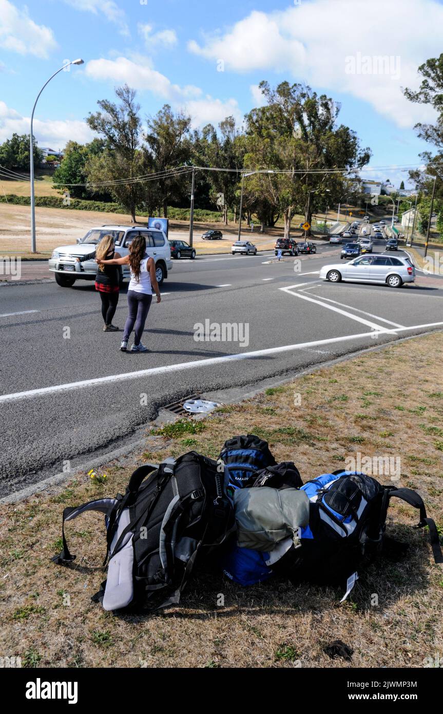 Dos jóvenes turistas se enganchan a hacer senderismo en una ajetreada carretera principal en Taupo, cerca del centro de la Isla del Norte de Nueva Zelanda. Foto de stock