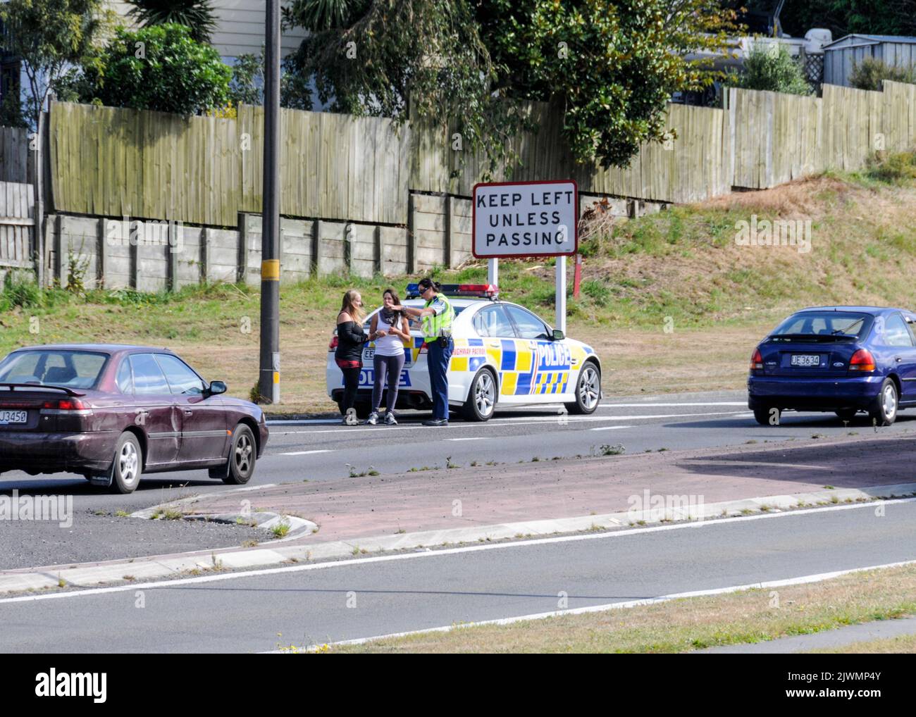 Un coche patrulla de la policía que pasa se ocupa de las dos jóvenes turistas que fueron enganche-senderismo en una carretera principal en Taupo, cerca del centro de Nueva Zelanda Foto de stock