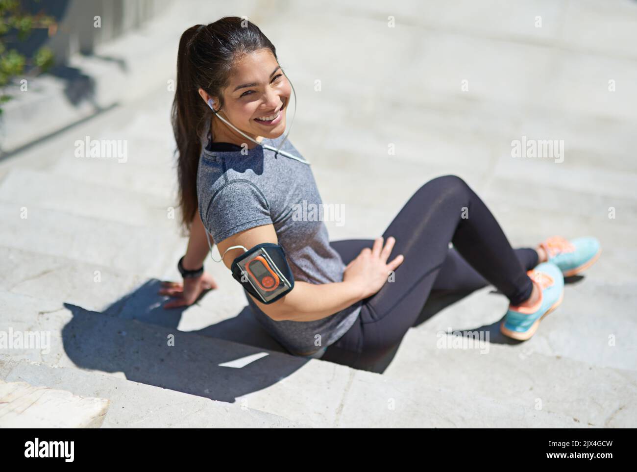 Ponerse más en forma con cada entrenamiento. Una mujer joven y deportiva que escucha música mientras está sentada en los escalones del exterior. Foto de stock