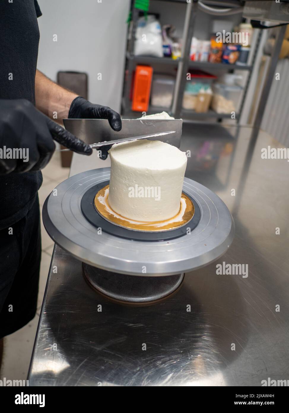Decorador con espátula y rascador para suavizar el cremoso de mantequilla en un pastel esmerilado Foto de stock