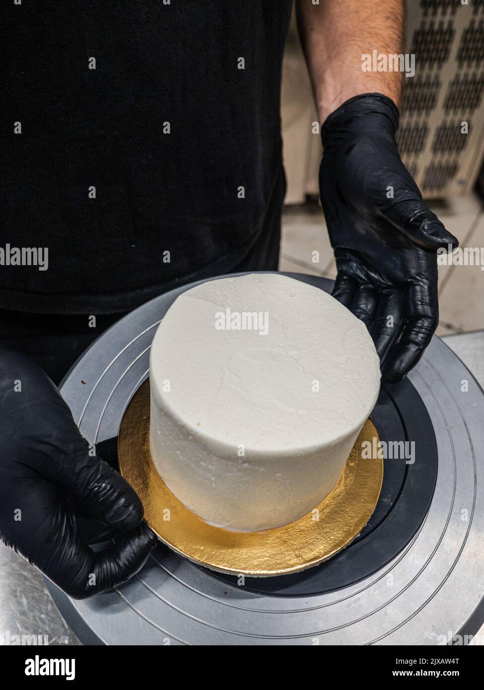 Decorador con espátula y rascador para suavizar el cremoso de mantequilla en un pastel esmerilado Foto de stock