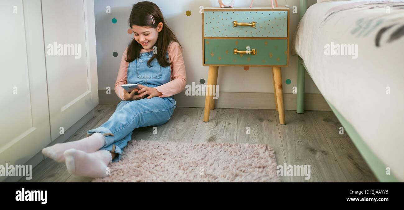 Chica riendo mirando el móvil sentado en el suelo Foto de stock