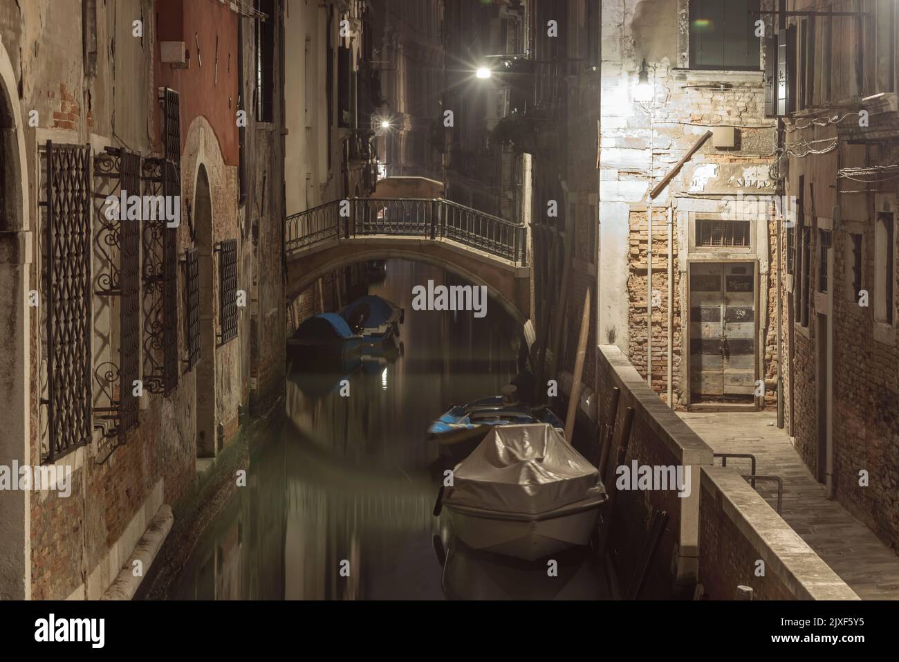 Estrecho canal de agua con barcos estacionados por la noche en Venecia Foto de stock