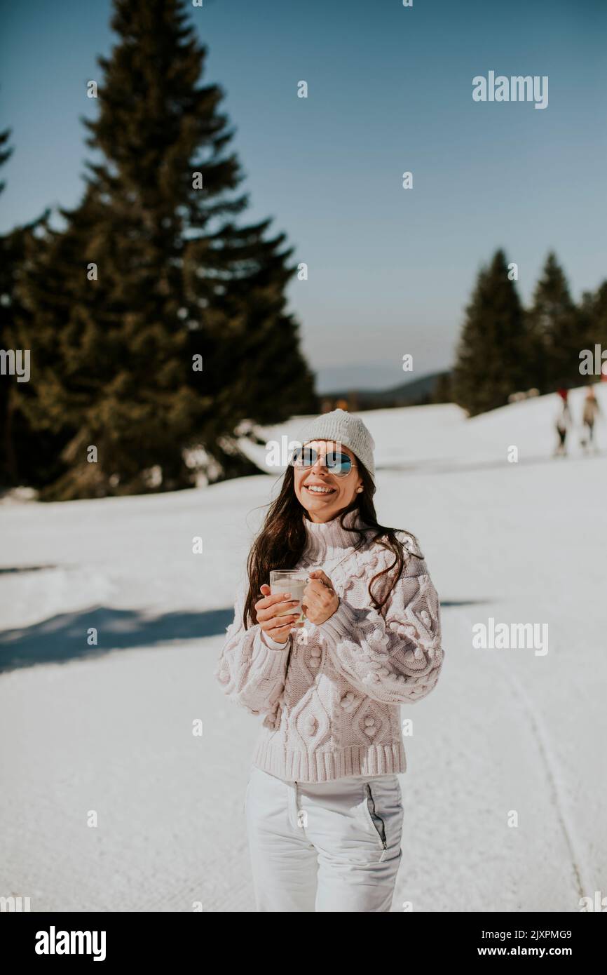Mujer joven bebiendo limonada en la pista de esquí de montaña en un soleado día de invierno Foto de stock