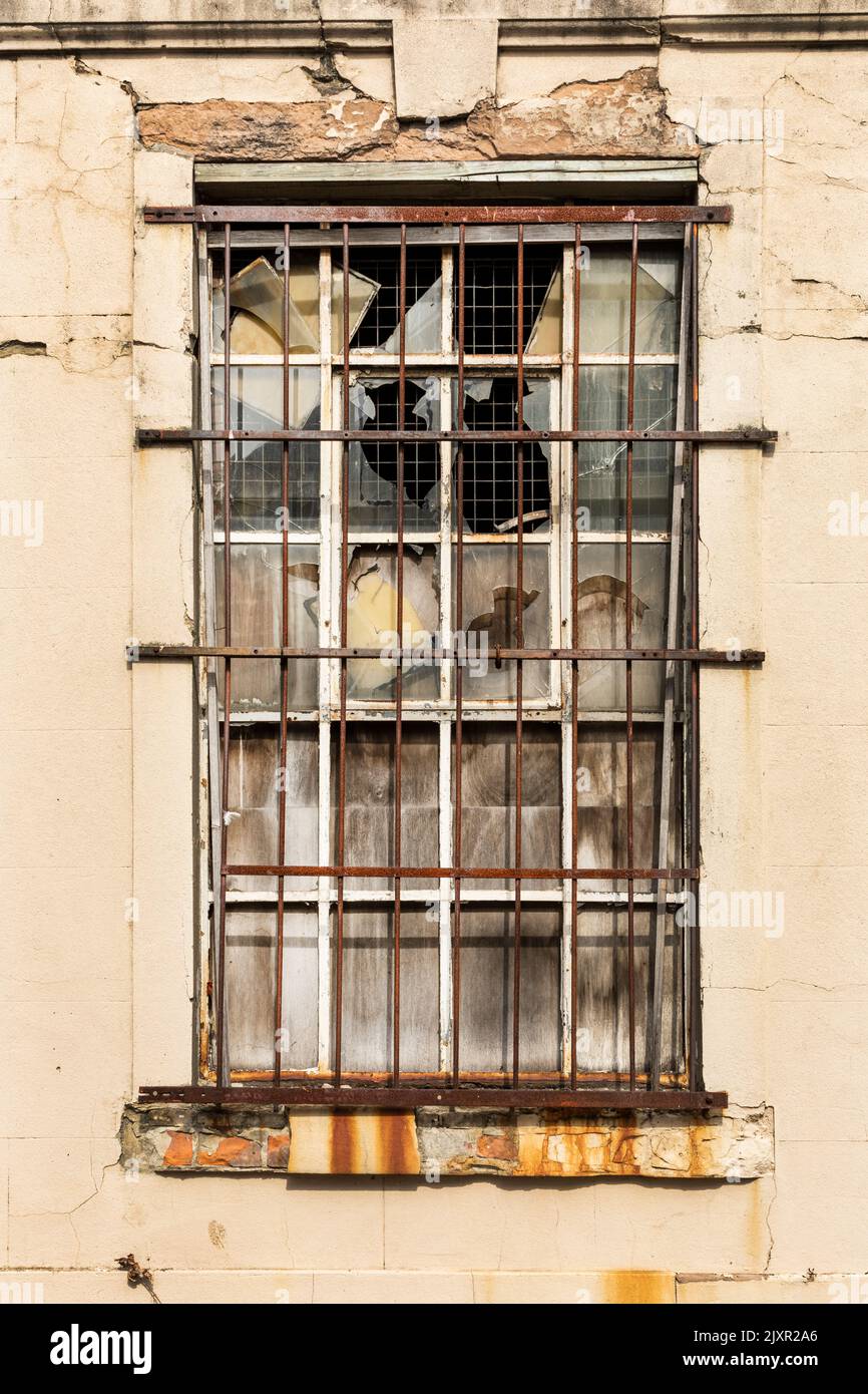 Una ventana barrada con vidrio roto Foto de stock