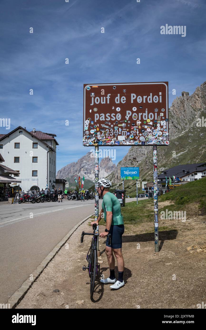 El ciclista se relaja bajo el signo que marca la cumbre del Paso de Pordoi (Passo Pordoi), Dolomitas, Italia. Foto de stock