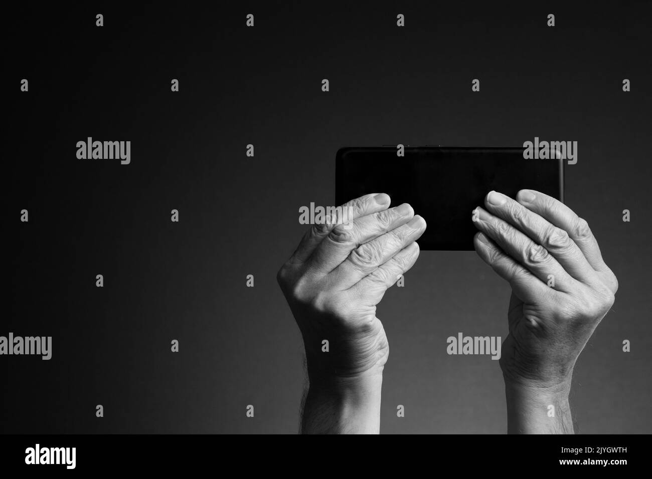 Imagen en blanco y negro, vista posterior de las manos del hombre sosteniendo el teléfono inteligente horizontalmente y los mensajes de texto o juegos aislados sobre un fondo oscuro con espacio de copia Foto de stock