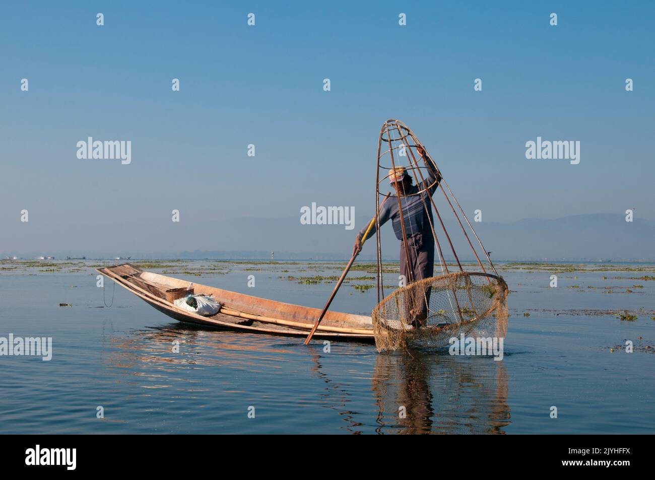 Birmania / Myanmar: Un pescador Intha de remo pierna muestra sus habilidades con una gran trampa cónica de peces en el lago Inle, estado de Shan. El Lago Inle es un lago de agua dulce situado en el estado de Shan. Es el segundo lago más grande de Myanmar y uno de los más altos a una altitud de 880 m (2.900 pies). La gente del Lago Inle (llamada Intha), unos 70.000 de ellos, viven en cuatro pueblos que bordean el lago, en numerosos pueblos pequeños a lo largo de las orillas del lago, y en el mismo lago. La población consiste predominantemente de Intha, con una mezcla de otros Shan, Taungyo, Pa-O (Taungthu), Danu, Kayah, Grupos étnicos de Danaw y Bamar. Foto de stock