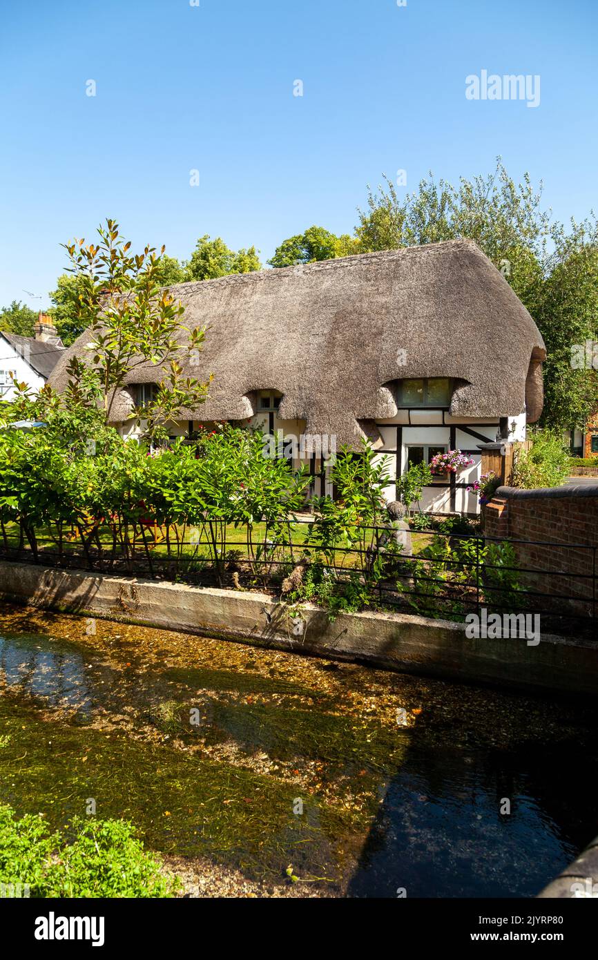 Una casa de campo con techo de paja junto a un pequeño río en Nether Wallop, Hampshire Foto de stock