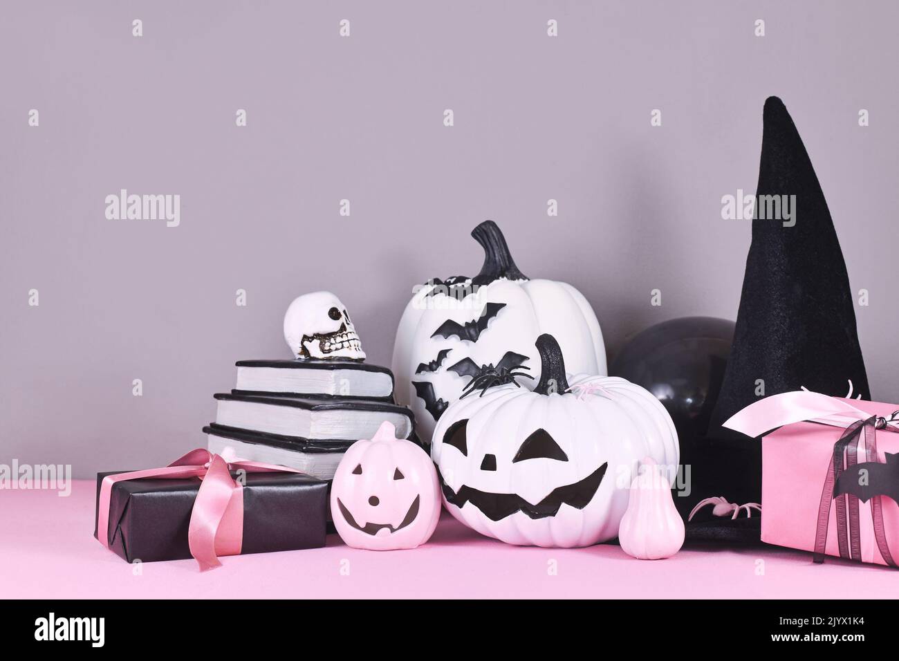 Decoración de Halloween rosa y blanco con calabazas en blanco y negro, sombrero de bruja y libros con hechizos sobre fondo gris Foto de stock