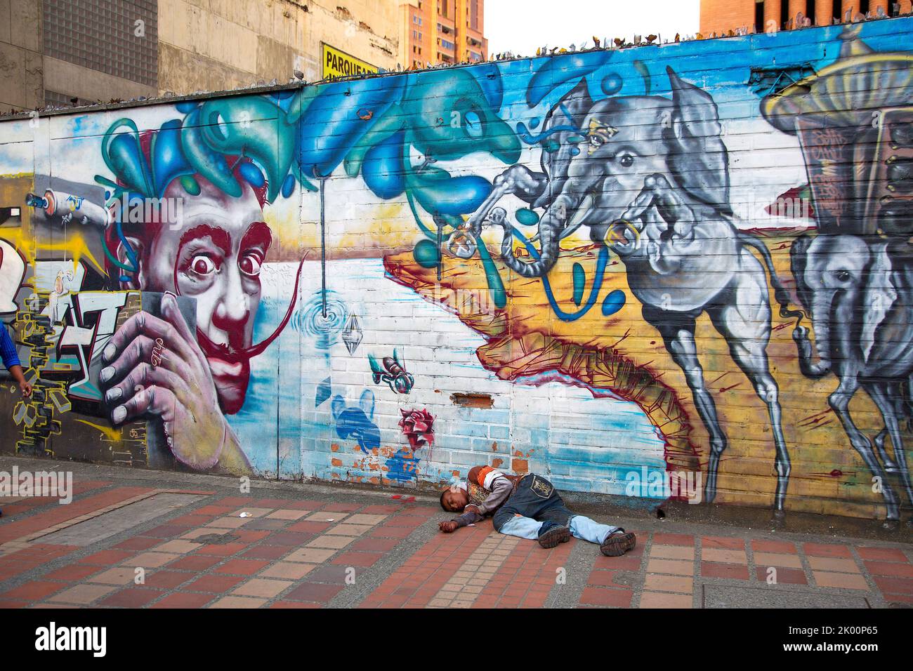 Colombia, Medellín, hombre sin hogar está acostado frente a una copia de Dalí que pintaba la pared. Foto de stock