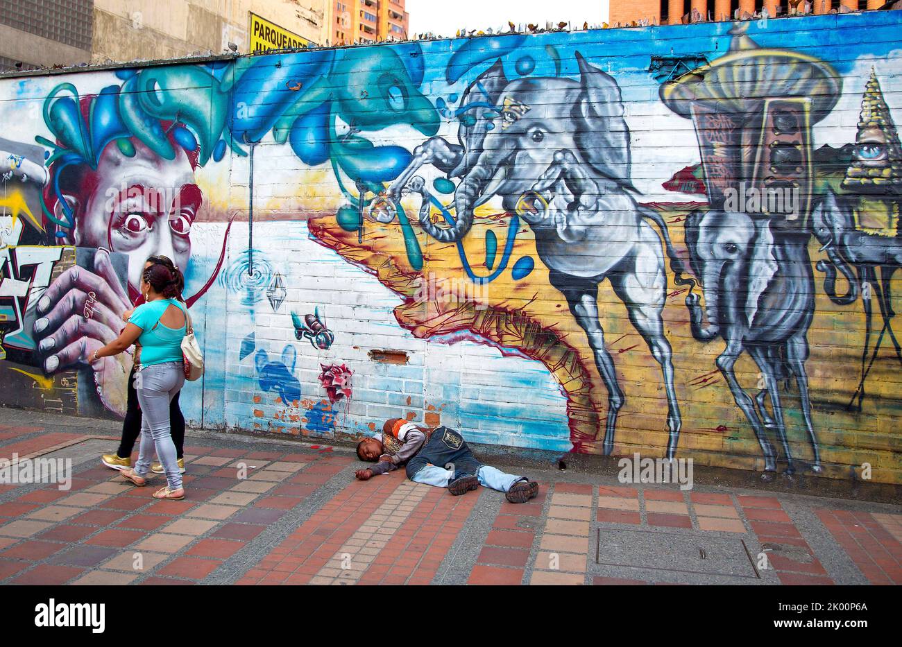 Colombia, Medellín, hombre sin hogar está acostado frente a una copia de Dalí que pintaba la pared. Foto de stock