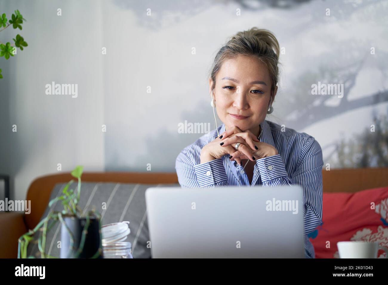 mujer asiática profesional madura que trabaja desde casa sentada en el sofá mirando el ordenador portátil Foto de stock