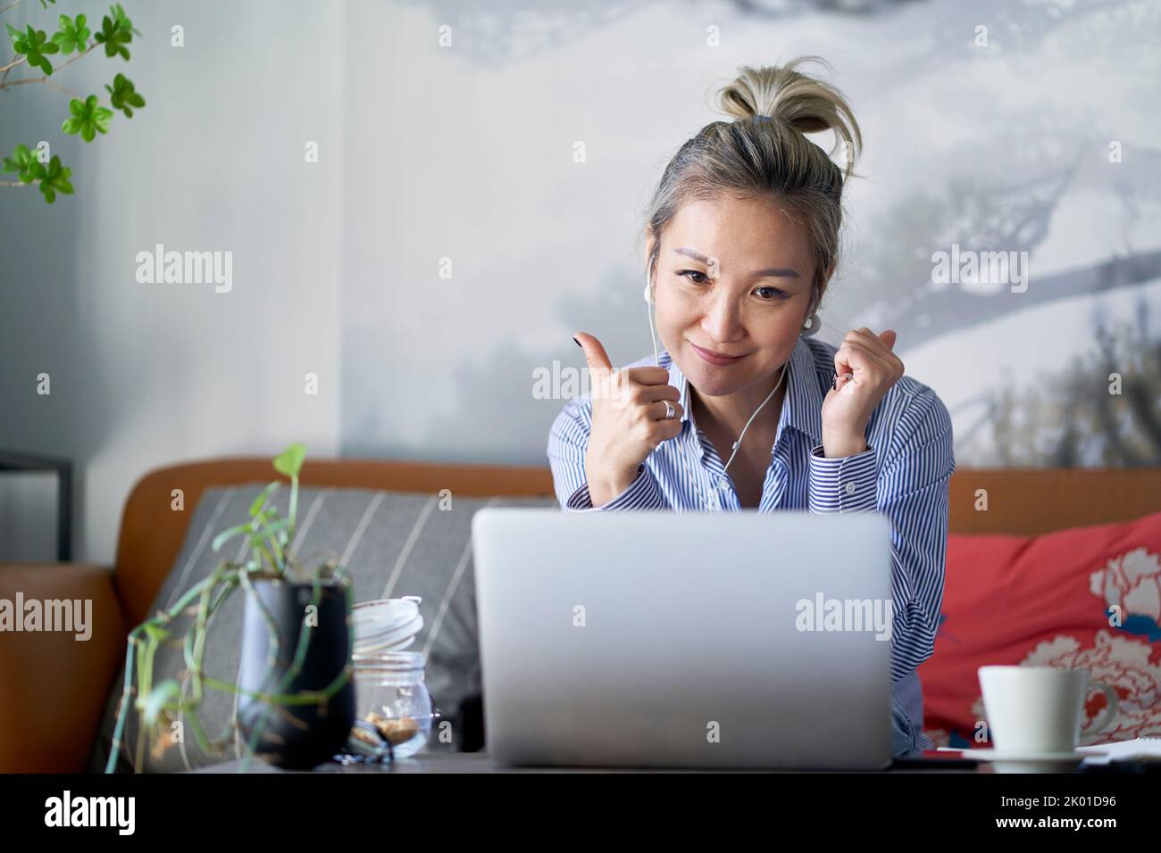 mujer asiática profesional madura que trabaja desde casa video chateando usando computadora portátil feliz y sonriente Foto de stock