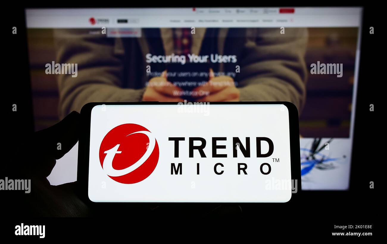 Persona que tiene un smartphone con el logotipo de la empresa de ciberseguridad Trend Micro Inc. En la pantalla delante del sitio web. Enfoque la pantalla del teléfono. Foto de stock