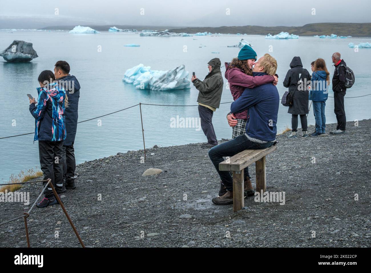 Una pareja besando mientras otros turistas toman fotografías de los icebergs en la laguna glacial Jokulsarlon, Islandia Foto de stock