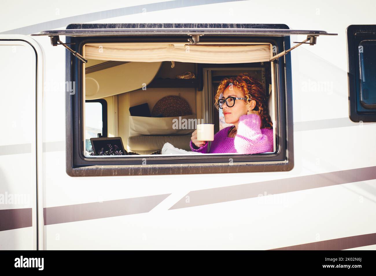 Vista exterior de una bonita mujer viajera que se relajaba dentro de su furgoneta campista vista desde la ventana. Vehículo reanting vacaciones y van vida de las personas de estilo de vida. Mujeres serenas en rv Foto de stock