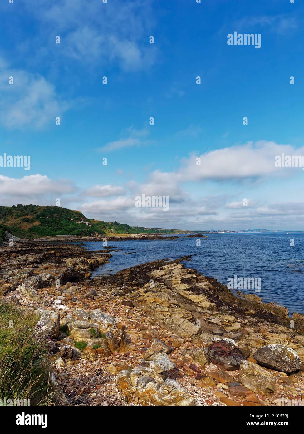 Los dedos irregulares de las rocas de arenisca sobresalen en la bahía de St Andrews desde Buddo Ness en la ruta costera de Fife en una mañana de verano. Foto de stock