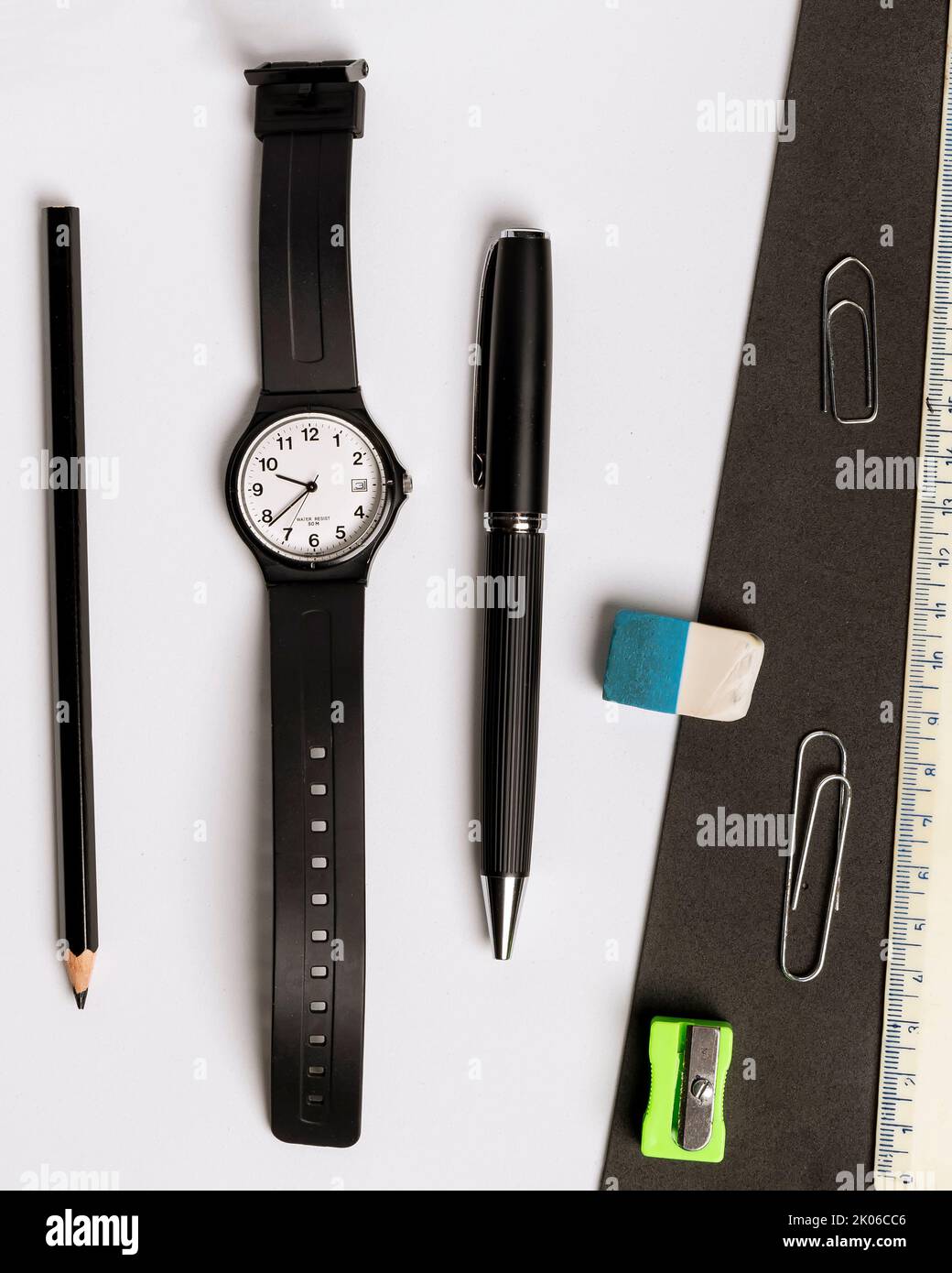 Bolígrafo, lápiz, borrador, sacapuntas, reloj de pulsera y regla sobre un fondo blanco y negro en contraste Foto de stock