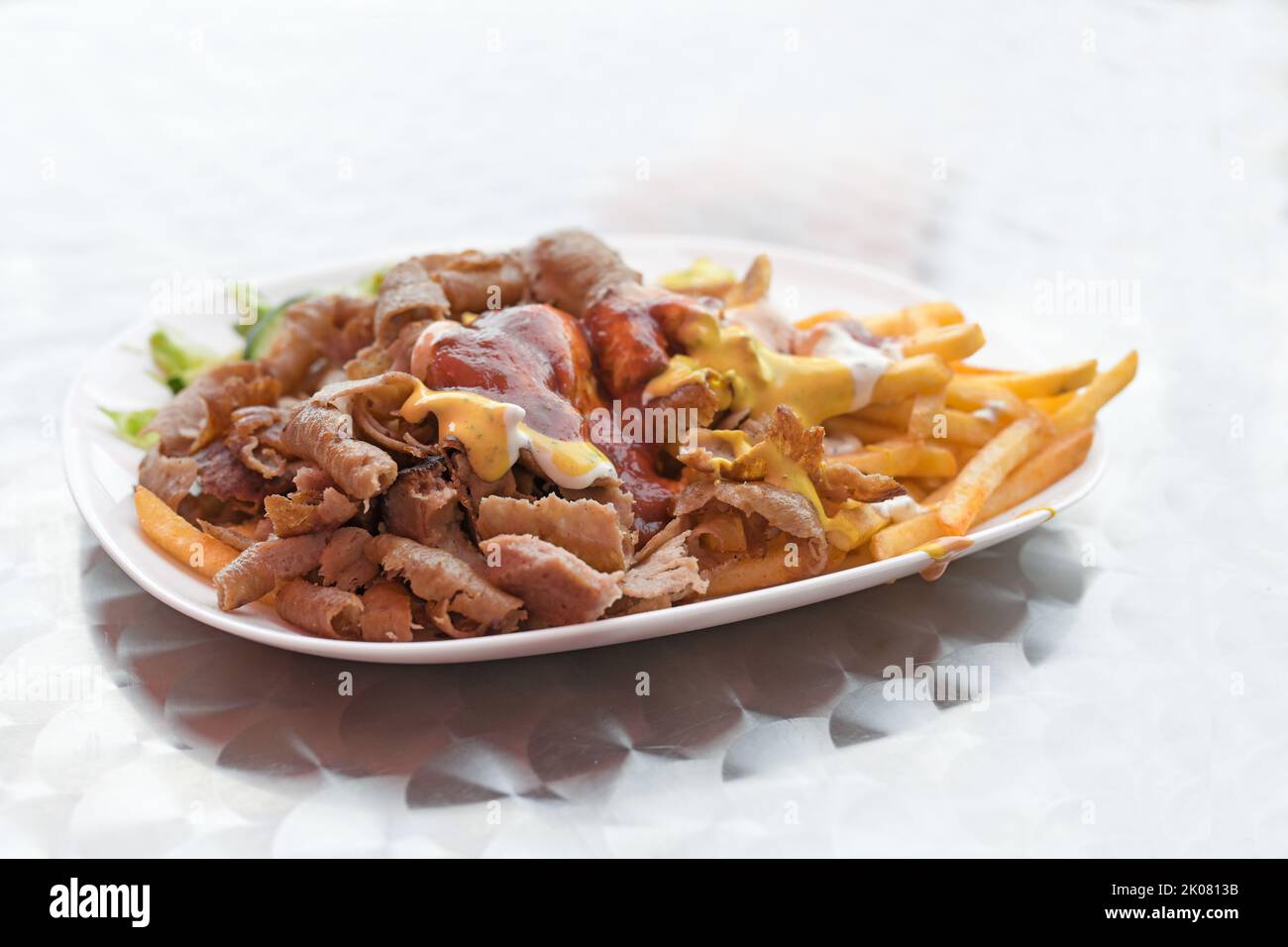 Doner kebab con patatas fritas y diversas salsas en un plato, comida rápida popular de la cocina turca, espacio de copiado, foco seleccionado, profundidad de campo estrecha Foto de stock