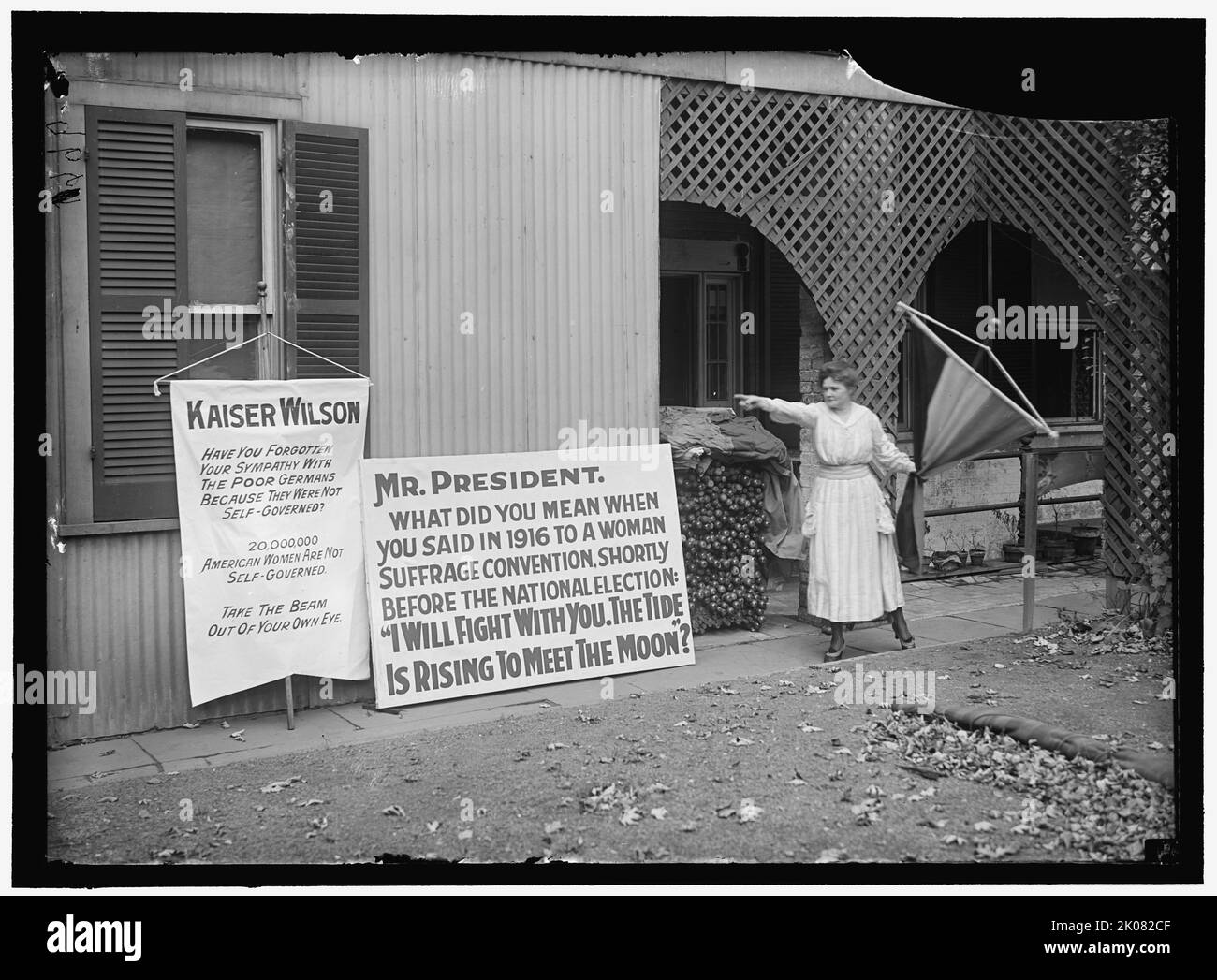 Pancartas de sufragio femenino, entre 1916 y 1918. Primera Guerra Mundial: Mujer señalando pancartas que decía: 'Kaiser [Woodrow] Wilson, ¿ha olvidado su simpatía con los pobres alemanes porque no eran autogobernados? 20.000.000 Las mujeres estadounidenses no son autogobernadas. Saque el haz del ojo'. Señor Presidente, ¿a qué se refería cuando en 1916 dijo a una convención sobre el sufragio femenino, poco antes de las elecciones nacionales?: «Me enfrentaré con usted. La marea sube para encontrarse con la Luna?'. Anote la pila de banderas y postes para las demostraciones. Las mujeres en los Estados Unidos ganaron el derecho legal a. Foto de stock