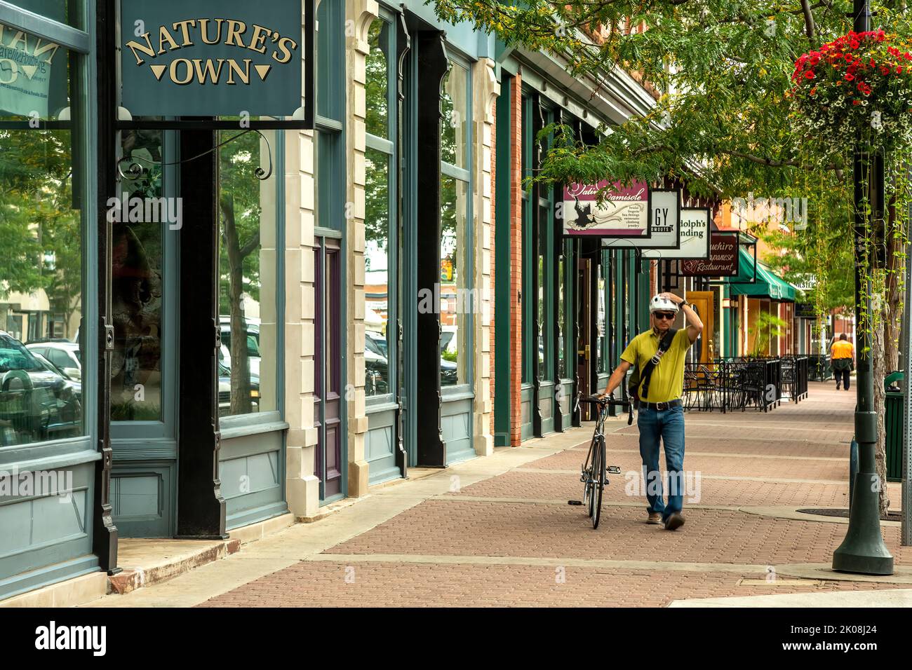 Hombre caminando su bicicleta por tiendas y tiendas, Old Town, Fort Collins, Colorado USA Foto de stock