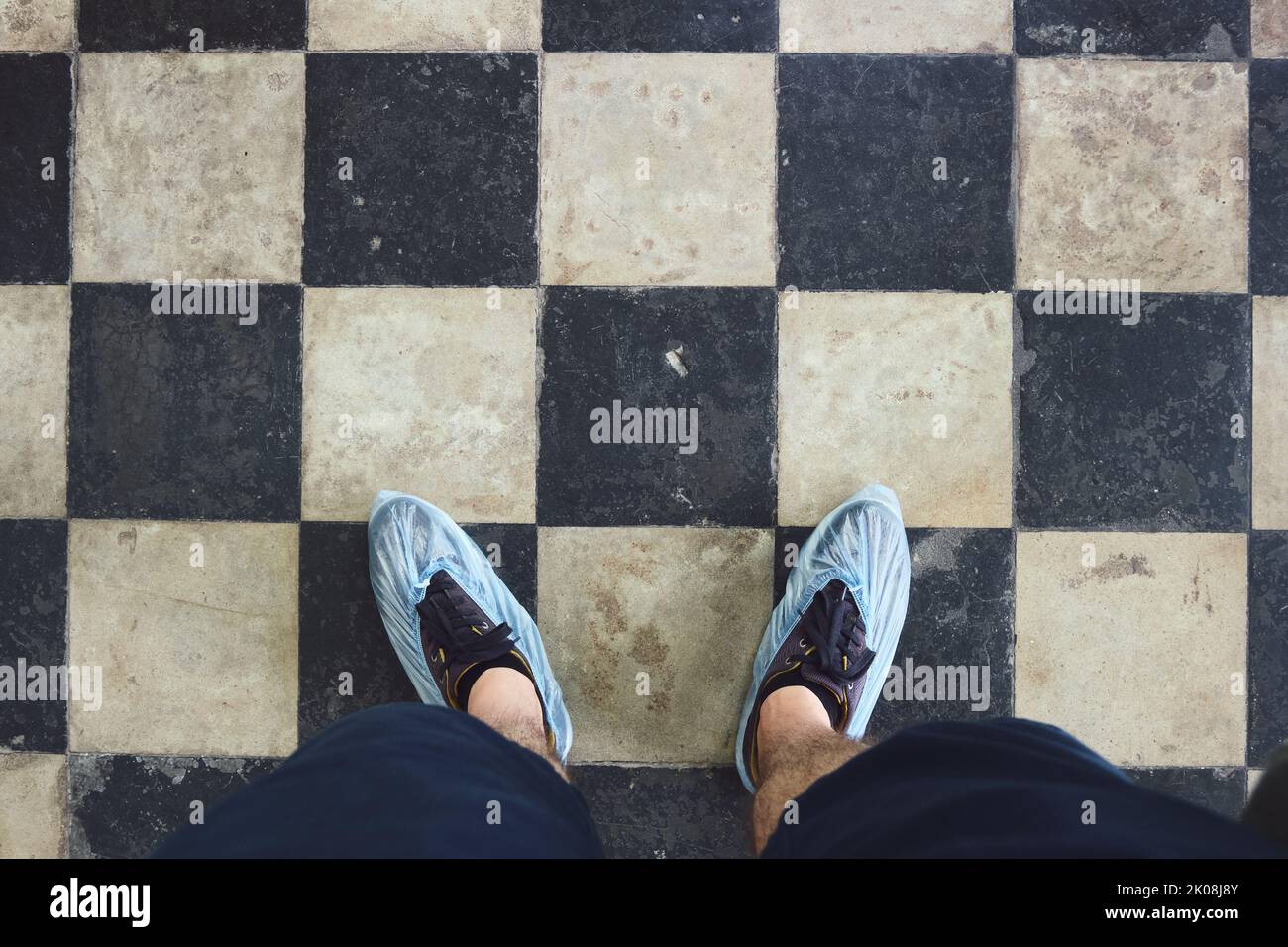 Hombre con cubrezapatos azules sobre botas de pie sobre azulejos. Piernas en cubrezapatos desechables contra el fondo del suelo cubierto con azulejos. Foto de stock