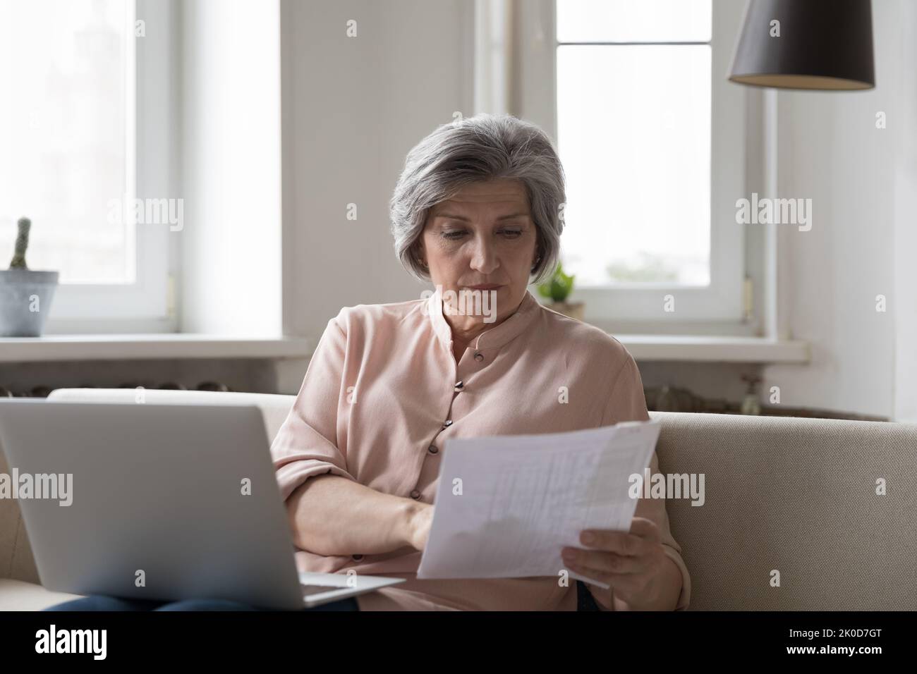 Mujer contadora senior enfocada en comprobar la factura en papel en el portátil Foto de stock