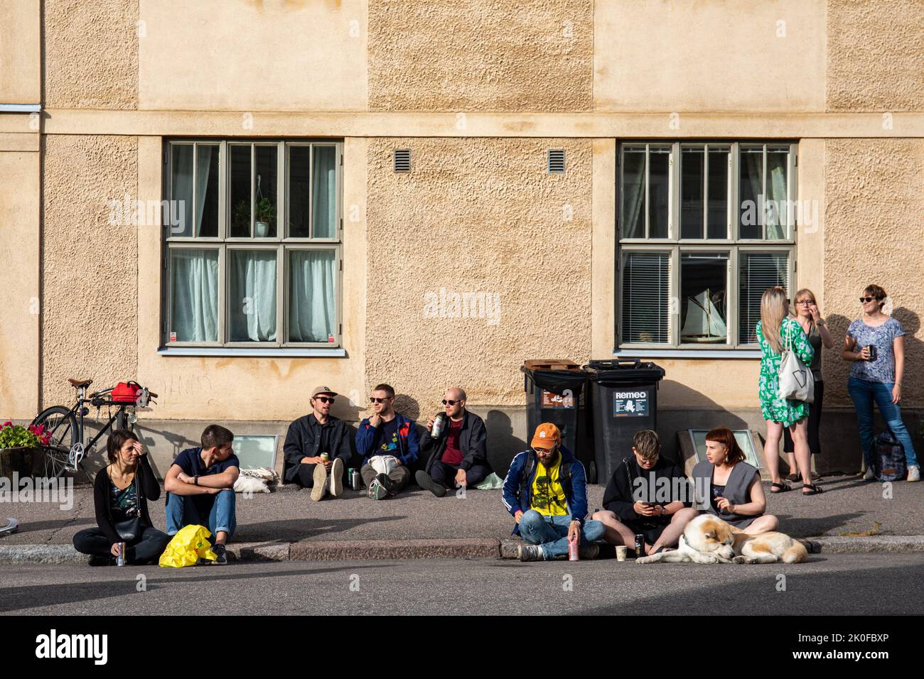 Personas sentadas en un bordillo y acera en Kallio Block Party 2022 en Alppila Distict de Helsinki, Finlandia Foto de stock