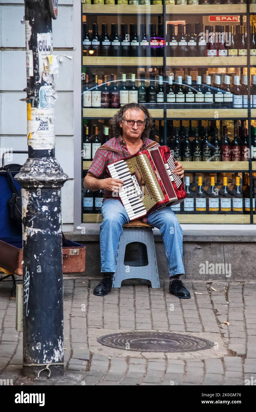 Julio 15 Tbilisi Georgia - Hombre sentado en el taburete frente a la tienda de vinos jugando acordeón en el casco antiguo Foto de stock