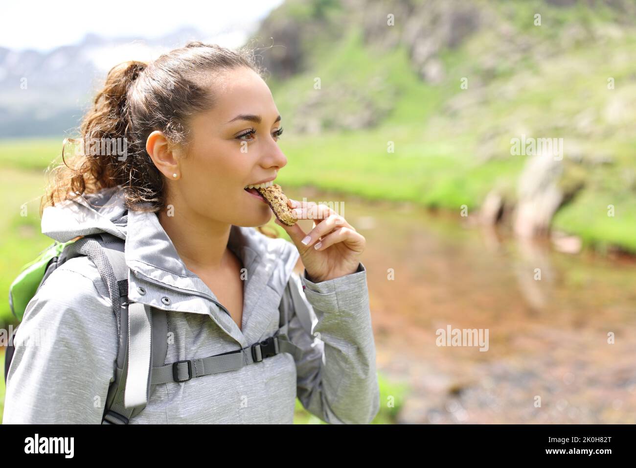 Excursionista feliz comiendo un bar de cereales caminando por la montaña Foto de stock