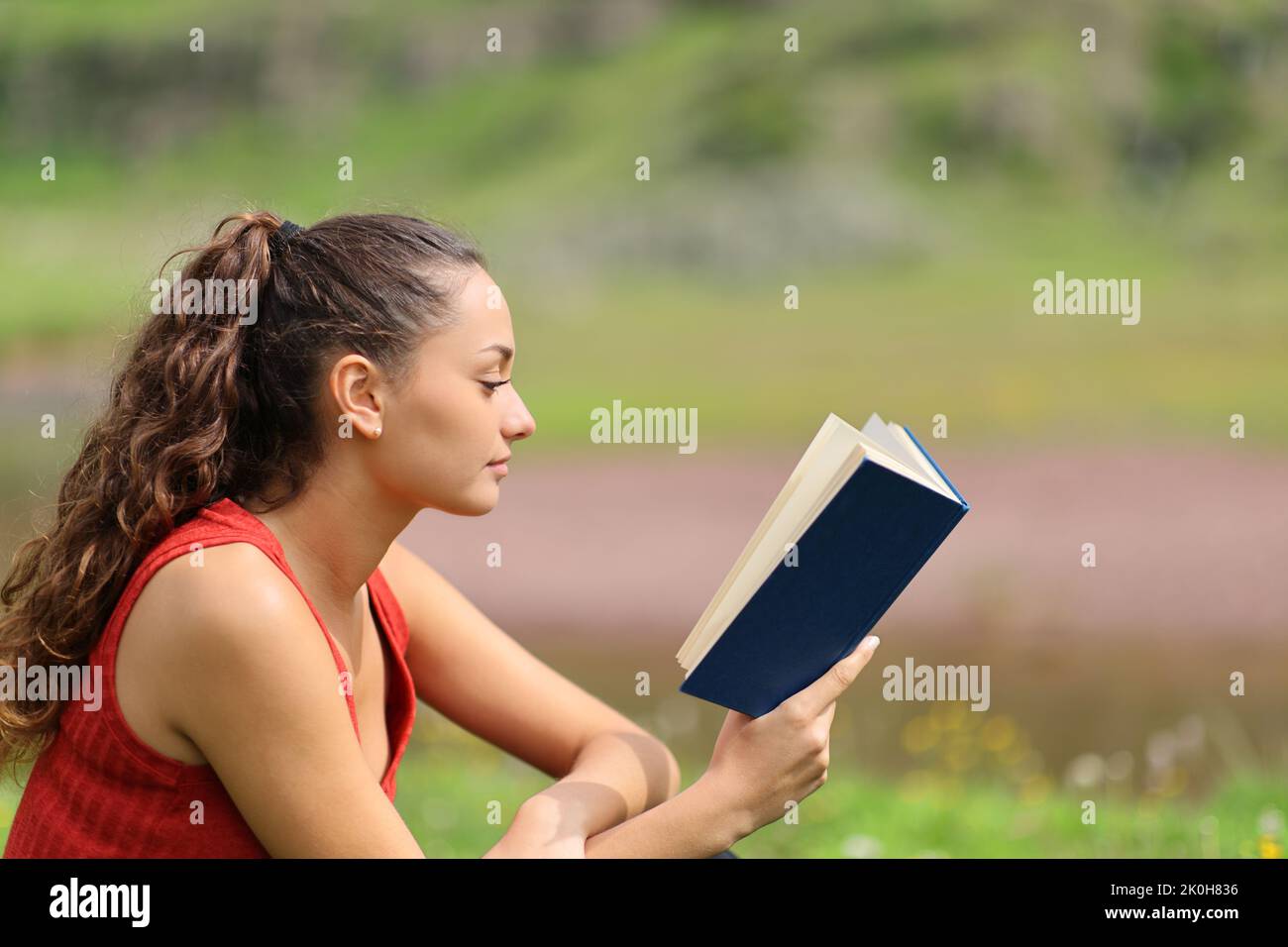 Retrato de vista lateral de una mujer consciente leyendo un libro relajado en la montaña Foto de stock