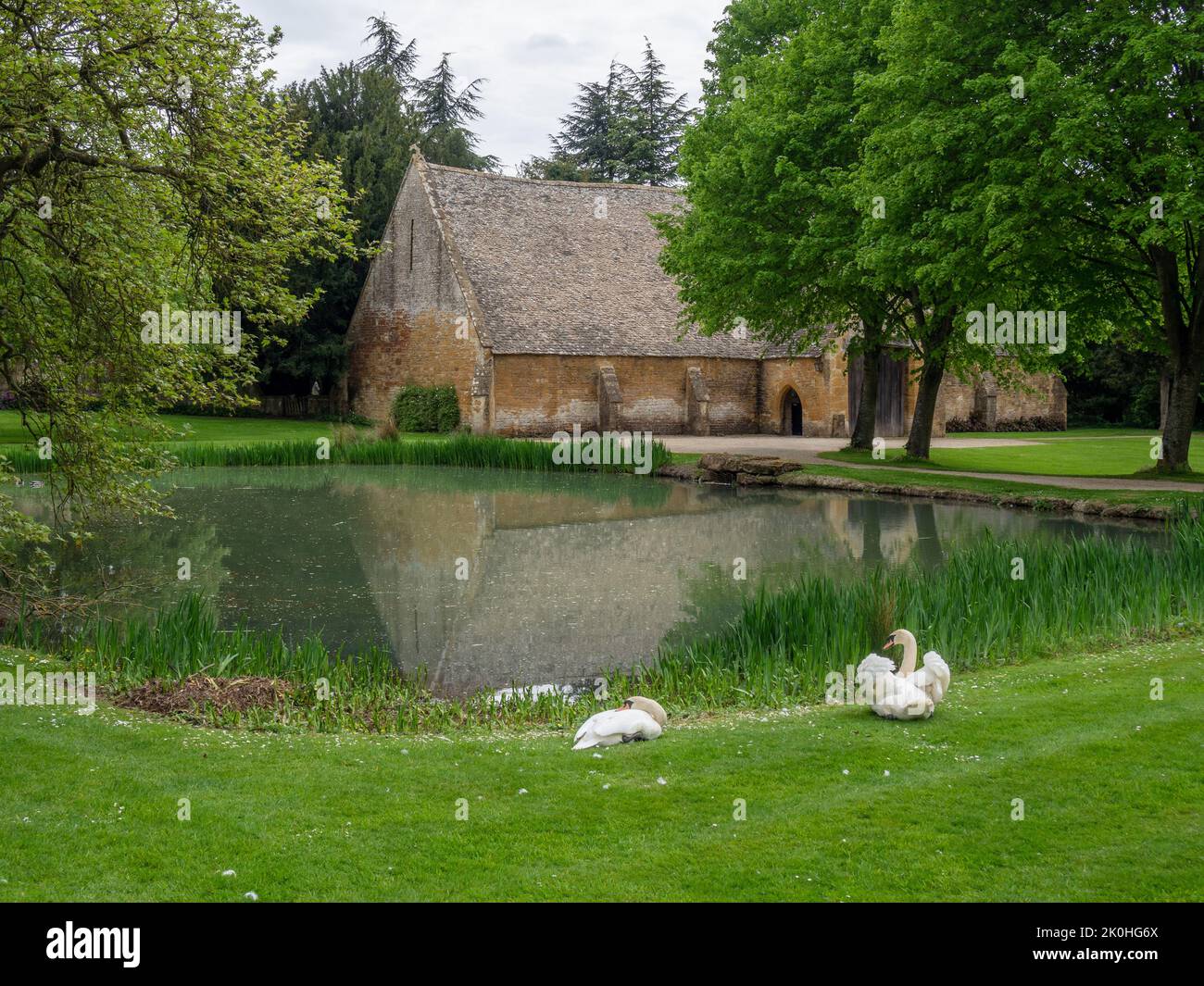Una vista del granero del diezmo medieval desde el estanque de patos, Stanway House, Gloucestershire, Reino Unido; ahora se utiliza como lugar para bodas Foto de stock