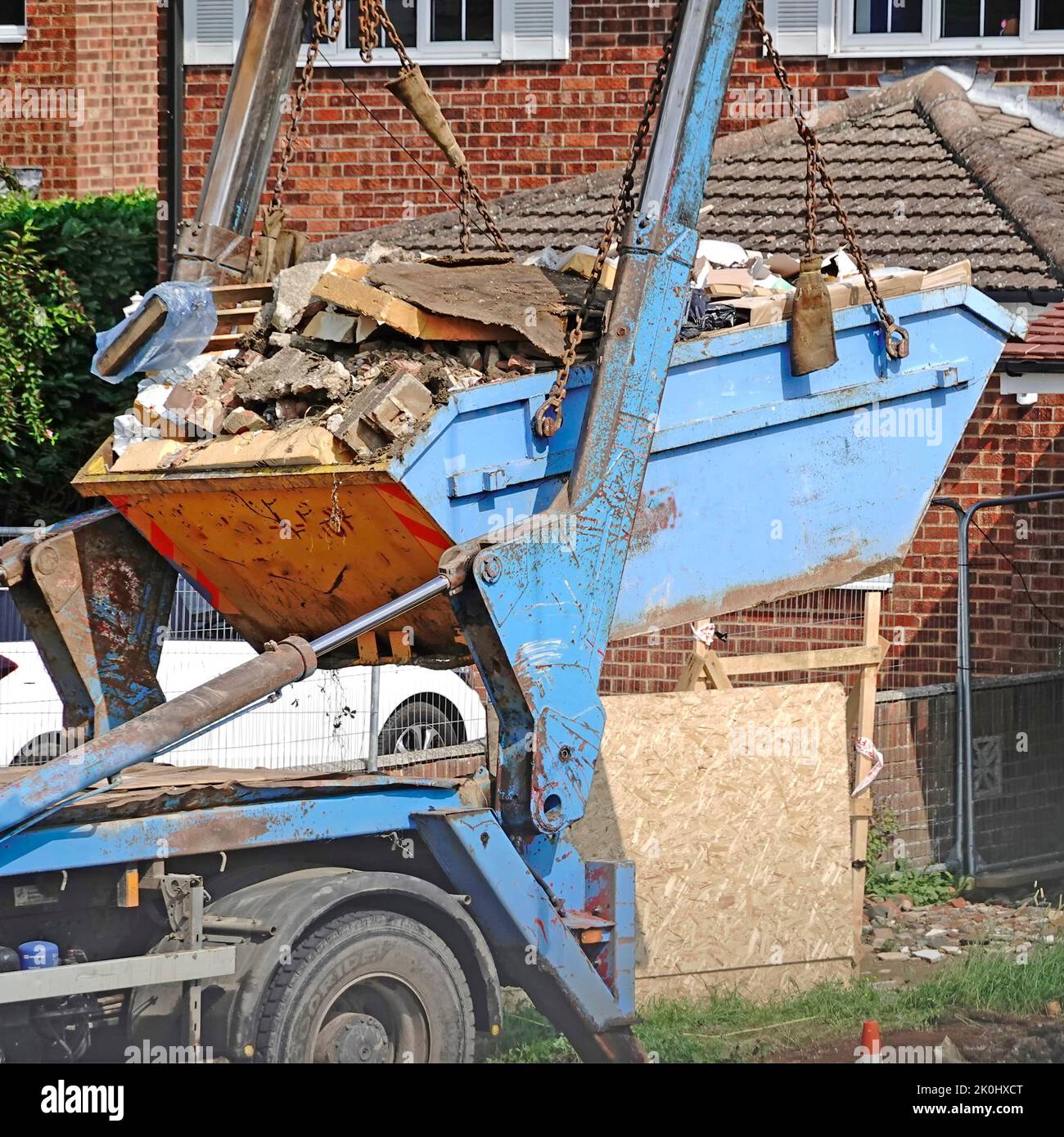 Se levantó un contenedor de basura completo del constructor del sitio compacto de construcción de bungalows hacia un camión cisterna para trasladarlo al vertedero de Inglaterra, Reino Unido Foto de stock