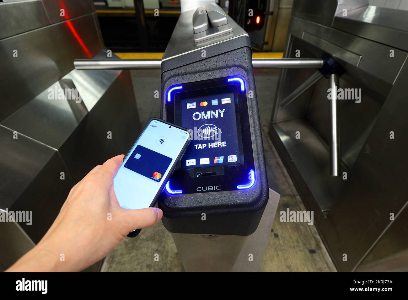 Un smartphone con Google Wallet toca un torniquete de metro de Nueva York equipado con un lector de pagos sin contacto OMNY que acepta pagos NFC Foto de stock