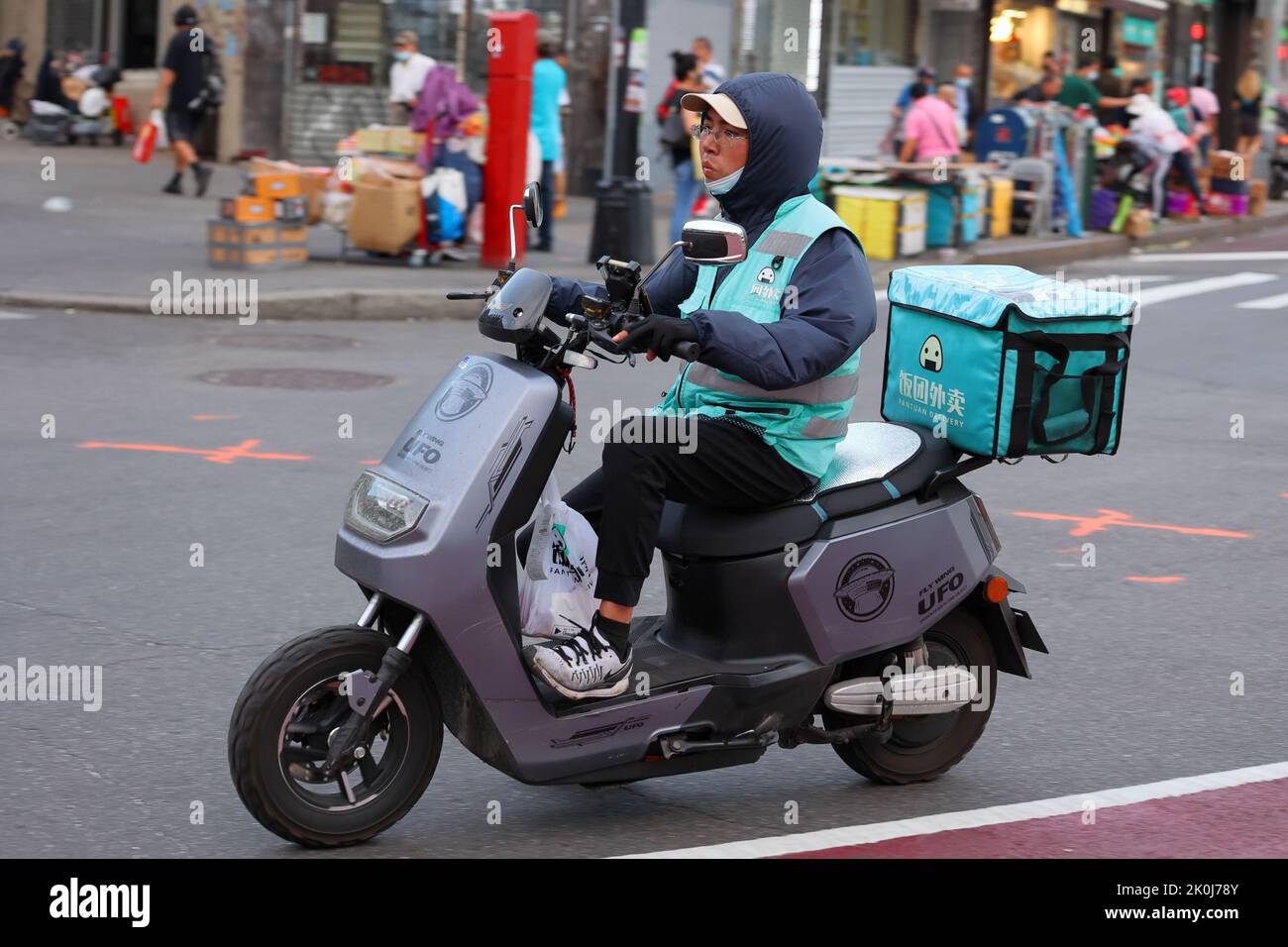 Una persona encargada de la entrega en un ciclomotor eléctrico en el centro de Flushing, Nueva York. Fantuan 飯糰外賣Asian entrega de alimentos Foto de stock