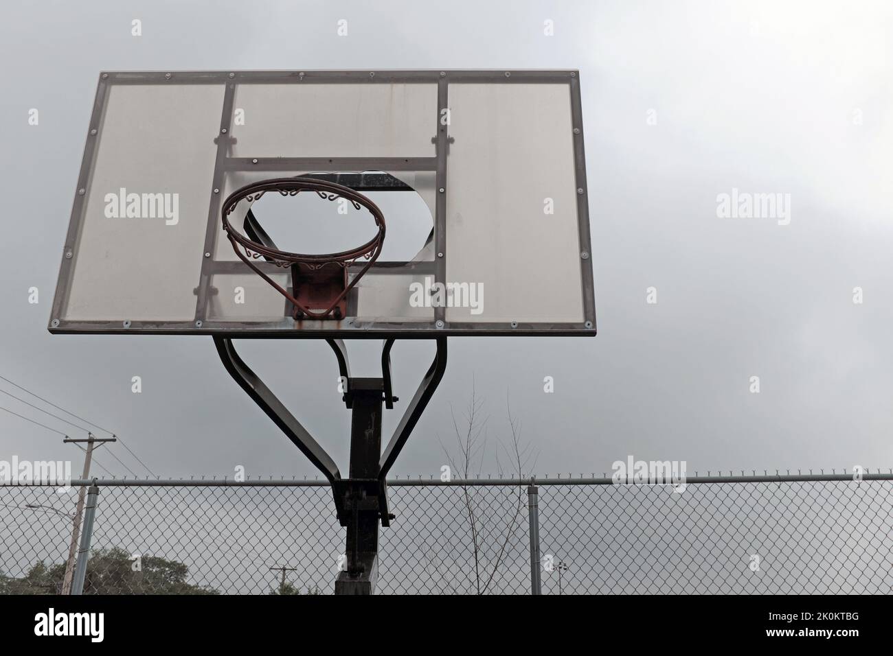 Un aro de baloncesto ruinoso sin red y tablero trasero roto se sienta descuidado en un patio de recreo. Foto de stock