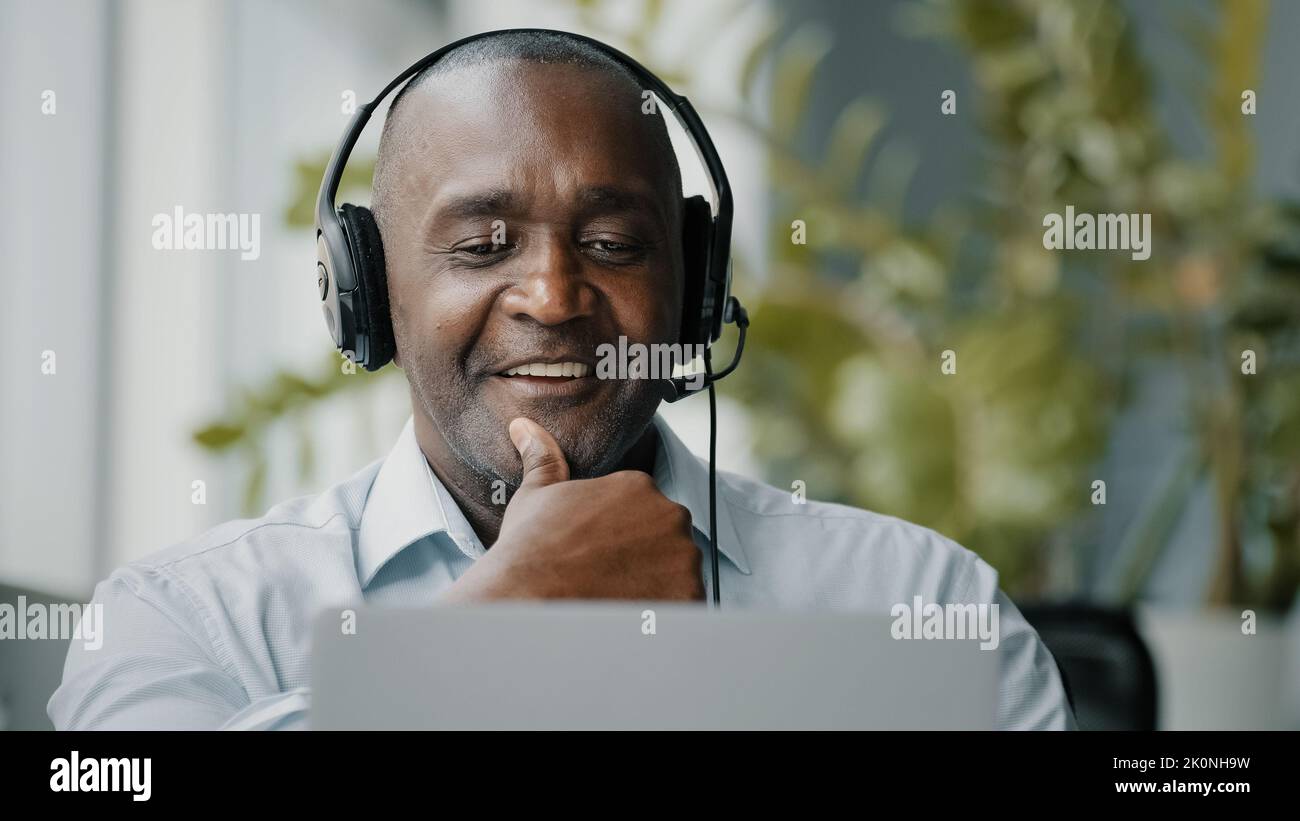 Hombre adulto mayor hombre africano experto partidario asesor que trabaja en la empresa de servicios de asistencia lleva auriculares mantener negociación distante con Foto de stock