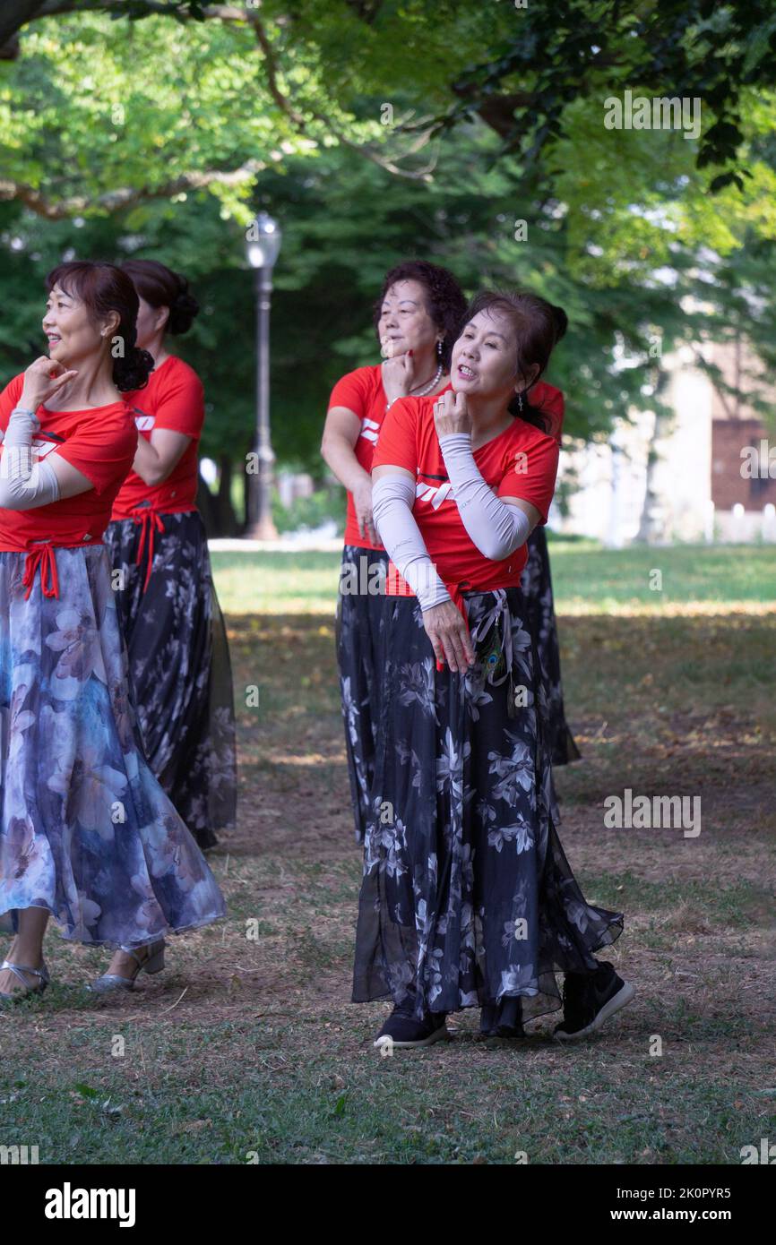 Forma parte de un gran grupo de mujeres chinas americanas en una clase de baile y ejercicio yuanji en un parque de Queens, Nueva York. Es una tradición matutina china. Foto de stock