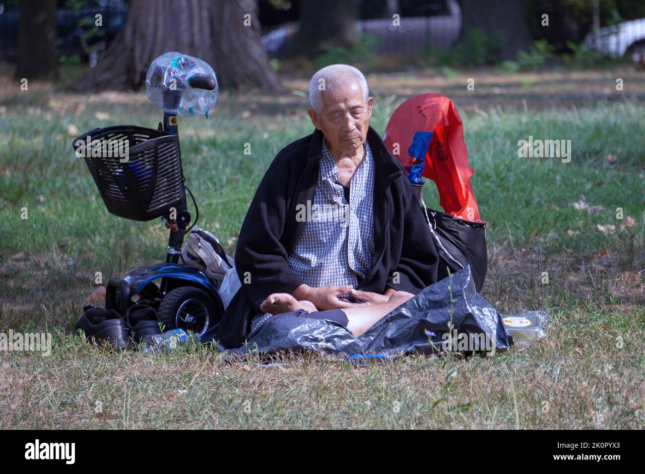 Un hombre sentado de 87 años hace ejercicios de movimiento lento de Falun Gong. En un parque en Queens, Nueva York, un lugar muy diverso. Foto de stock