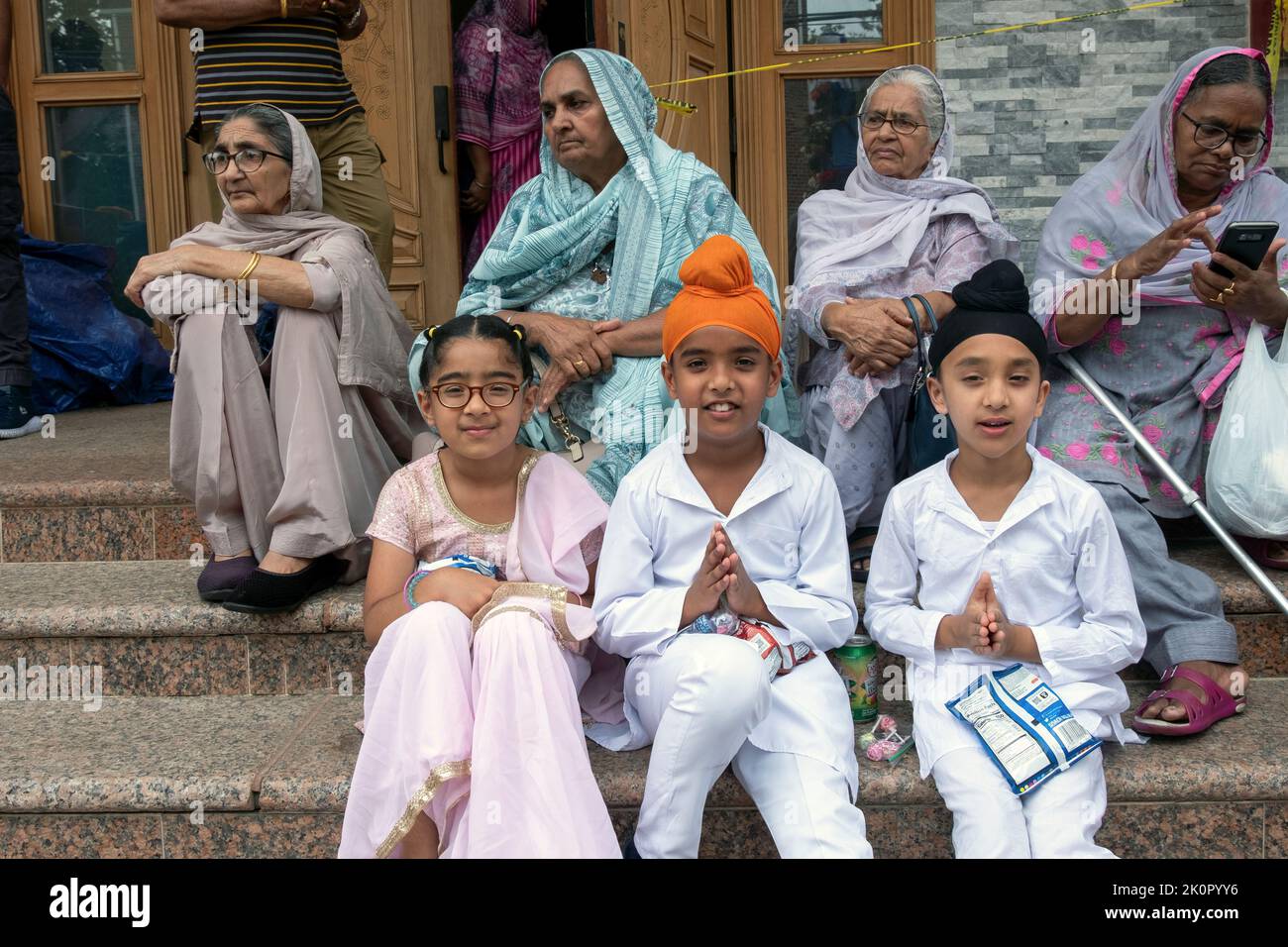 En los escalones del Centro Cultural Sikh, los niños y las mujeres de la tercera edad esperan el comienzo del Desfile Nagar Kirtan. En Richmond Hill, Queens, Nueva York Foto de stock