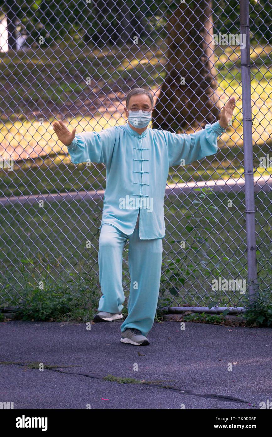 Un hombre de mediana edad con una máscara y un traje de Tai Chi dirige una clase matutina en un parque en Queens, Nueva York. Foto de stock